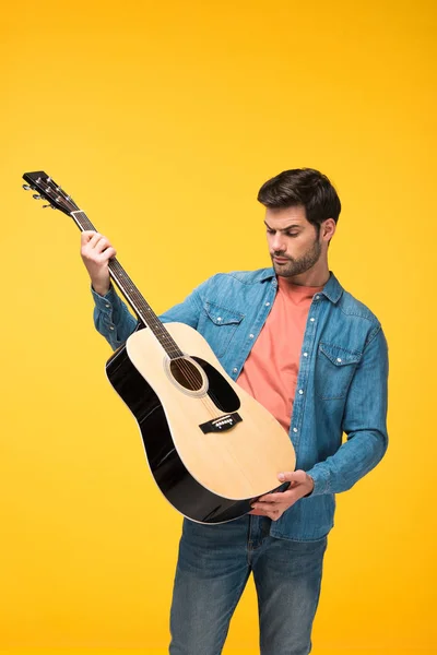 Bonito homem segurando guitarra acústica isolado no amarelo — Fotografia de Stock