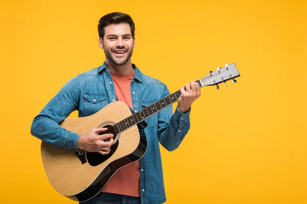 Guapo sonriente hombre tocando la guitarra acústica aislado en amarillo - foto de stock