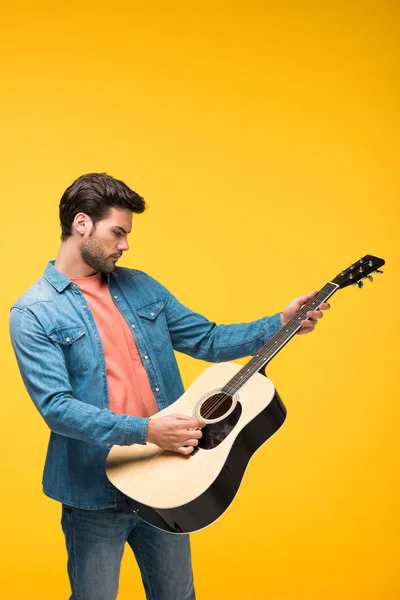 Красивый мужчина играет на акустической гитаре на желтом — стоковое фото
