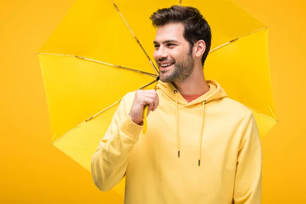 Handsome smiling man holding umbrella isolated on yellow — Stock Photo