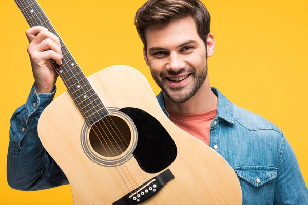 Guapo feliz hombre sosteniendo guitarra acústica aislado en amarillo - foto de stock