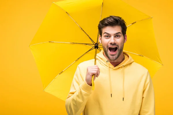 Красивий збуджений чоловік тримає парасольку ізольовано на жовтому — стокове фото