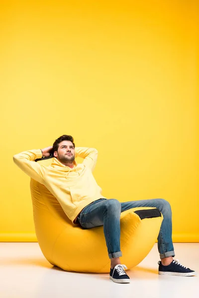 Uomo con le mani dietro la schiena rilassante sulla sedia sacchetto di fagioli su giallo — Foto stock