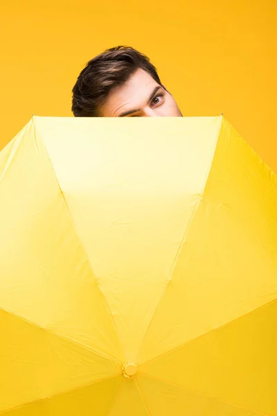 Handsome man covering face with umbrella isolated on yellow — Stock Photo