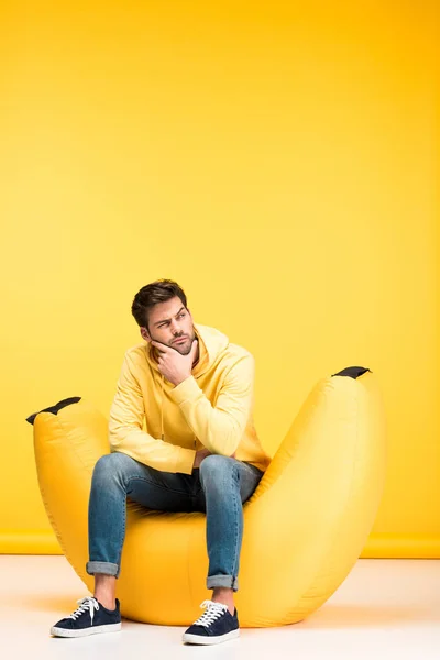 Pensive man on bean bag chair touching chin on yellow — Stock Photo