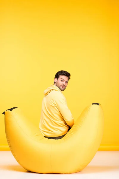 Hombre sentado en silla de la bolsa de frijol en amarillo y mirando a la cámara - foto de stock