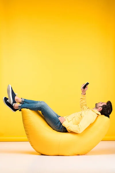 Man on bean bag chair taking selfie on smartphone on yellow — Stock Photo