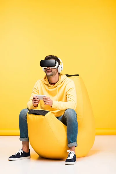 Man on bean bag chair with smartphone in virtual reality headset on yellow — Stock Photo