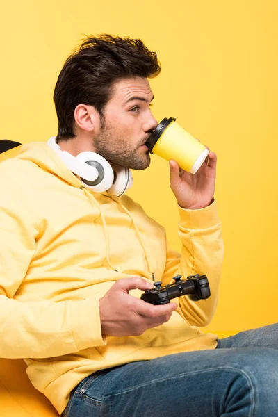 KYIV, UKRAINE - APRIL 12: man drinking coffee to go and playing Video Game isolated on yellow — Stock Photo