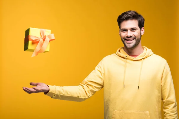 Schöner lächelnder Mann wirft Luftgeschenk auf gelb — Stockfoto