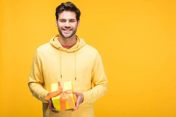 Guapo sonriente hombre sosteniendo regalo aislado en amarillo - foto de stock