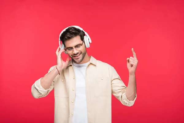 Sonriente hombre guapo en auriculares apuntando con el dedo aislado en rosa - foto de stock
