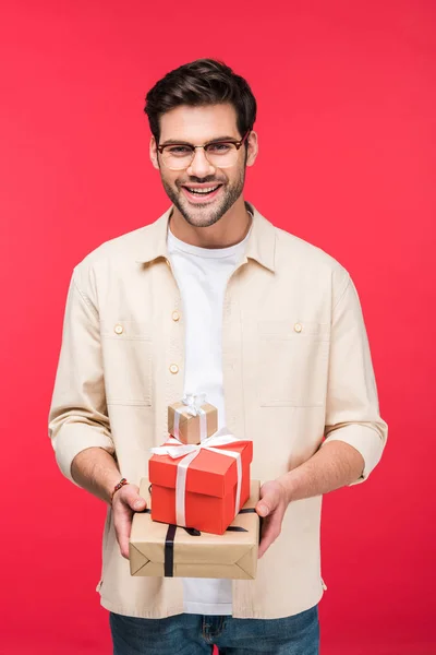 Guapo sonriente hombre sosteniendo regalos aislado en rosa - foto de stock