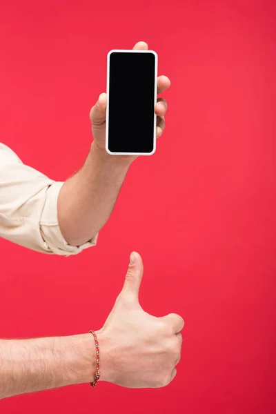 Обрезанный вид человека, держащего смартфон с пустым экраном и делающего большой палец вверх вывеску Изолированный на розовый — стоковое фото