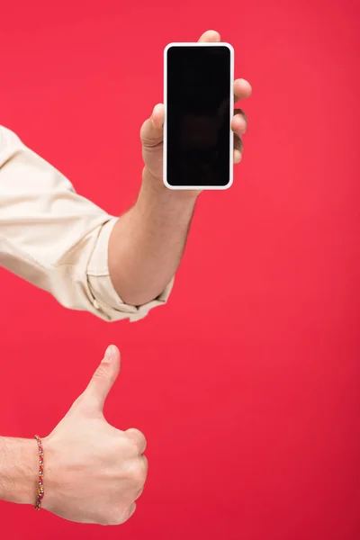 Vista recortada del hombre sosteniendo el teléfono inteligente con la pantalla en blanco y haciendo el pulgar hacia arriba signo aislado en rosa - foto de stock