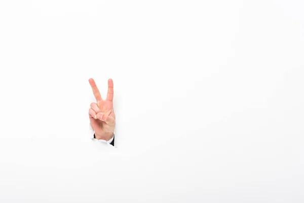 Hombre mostrando signo de paz desde el agujero en la pared de papel en blanco con espacio de copia - foto de stock