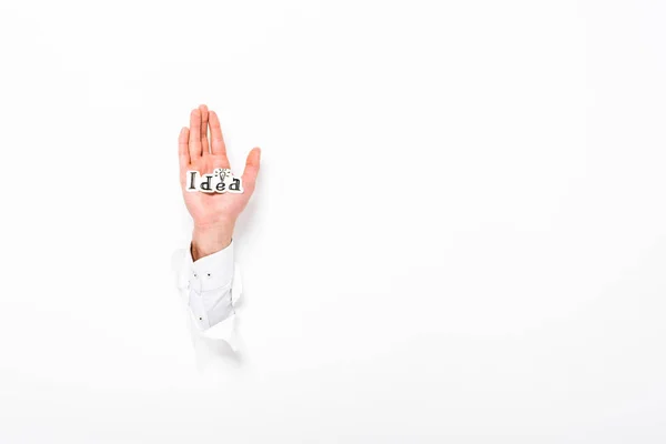 Cropped view of man holding paper with idea word from hole in wall on white with copy space — Stock Photo