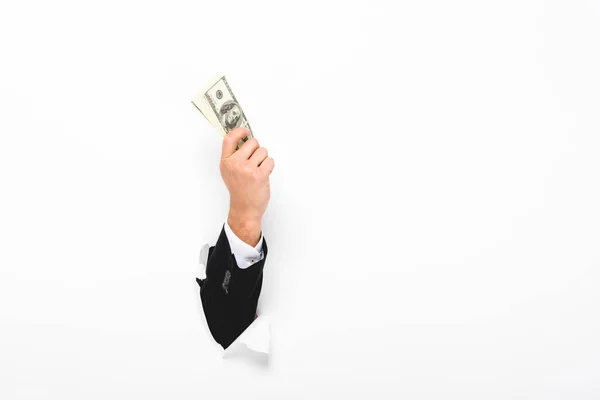 Cropped view of man holding money through hole in paper wall on white with copy space — Stock Photo