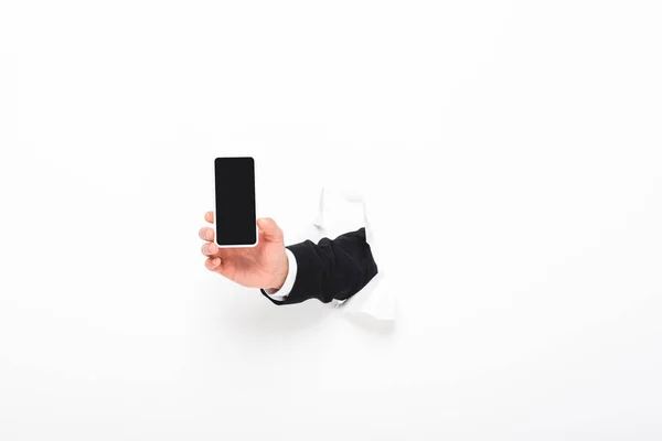 Vista recortada del hombre sosteniendo el teléfono inteligente desde el agujero en la pared en blanco con espacio de copia - foto de stock