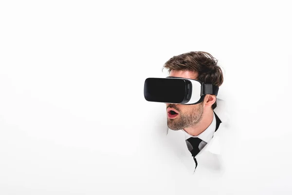 Schockierter Mann in Virtual-Reality-Headset hinter Loch in Wand auf weiß — Stockfoto