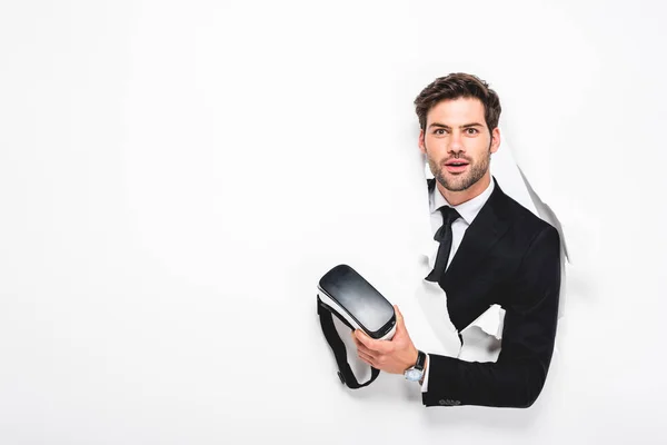 Surprised man holding Virtual reality headset behind hole in wall on white — Stock Photo