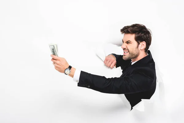 Hombre de negocios enojado sosteniendo billetes de dólar detrás de un agujero en la pared de papel en blanco - foto de stock