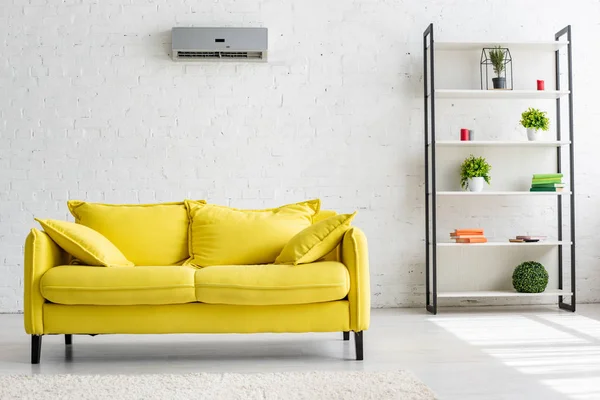 Geräumiges Wohnzimmer mit Klimaanlage an weißer Wand, gelbem Sofa und Ablage — Stockfoto