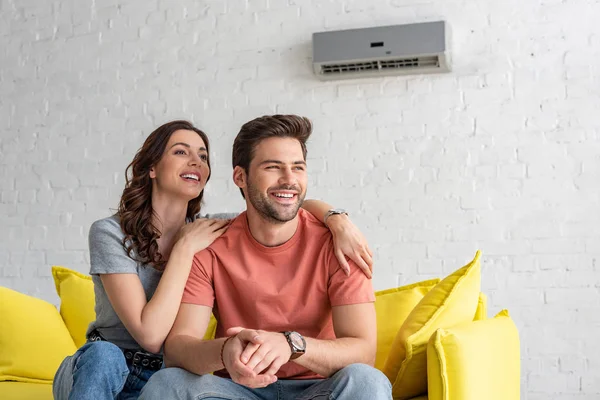 Happy couple sitting on yellow sofa under air conditioner at home — Stock Photo