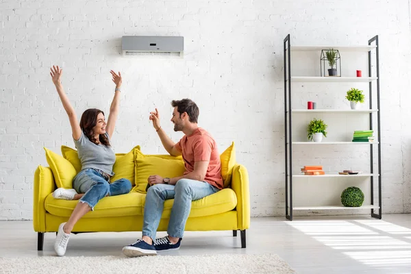 Happy man and woman talking while sitting on yellow sofa under air conditioner at home — Stock Photo