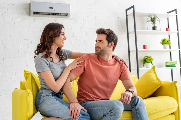 Glückliche junge Frau umarmt gutaussehenden Freund, während sie auf dem Sofa unter Klimaanlage sitzt — Stockfoto