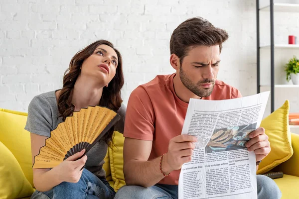 Woman with hand fan and man with newspaper suffering from heat at home — Stock Photo