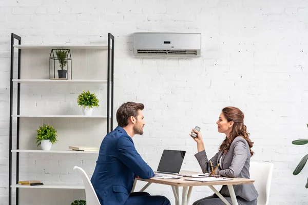 Socios de negocios hablando mientras están sentados en el lugar de trabajo bajo el aire acondicionado - foto de stock
