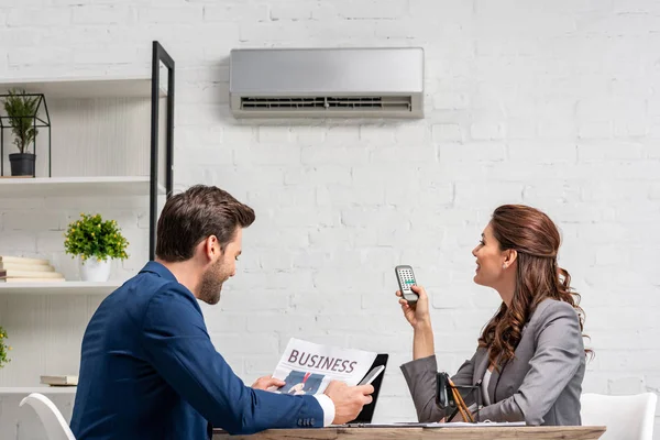 Businessman reading business newspaper while sitting at desk near pretty woman holding remote control — Stock Photo