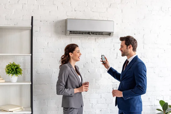 Sonrientes empresarios hablando mientras están de pie bajo el aire acondicionado en la oficina - foto de stock