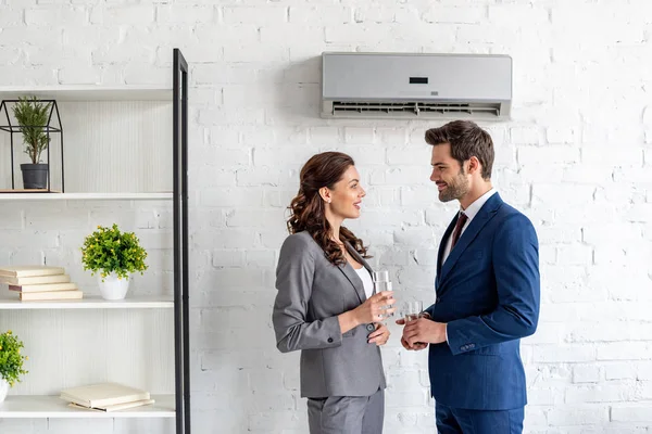 Young smiling businesspeople talking while standing under air conditioner with glasses of water — Stock Photo