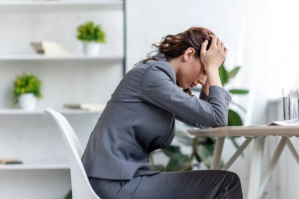 Femme d'affaires épuisée tenant les mains près de la tête tout en souffrant de la tête au bureau — Photo de stock