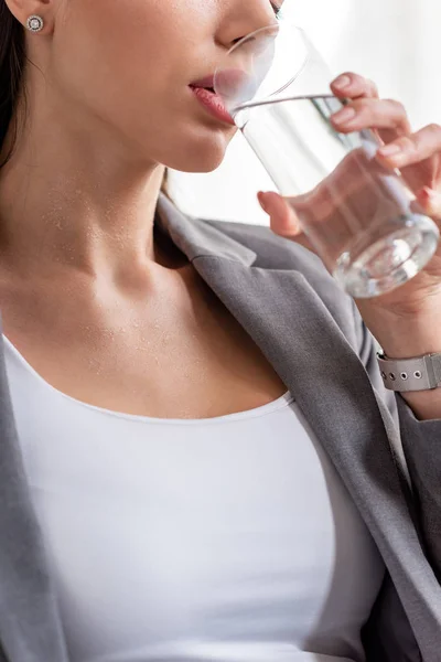 Vista recortada de la mujer joven que sufre de agua potable de vidrio, mientras que sufre de calor en blanco - foto de stock