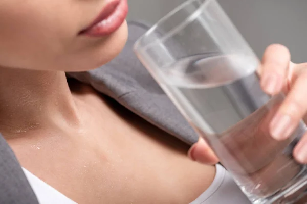 Vista recortada de una mujer joven sosteniendo un vaso de agua mientras sufre de calor en gris - foto de stock
