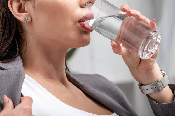Partial view of young businesswoman drinking water from glass while suffering from heat — Stock Photo