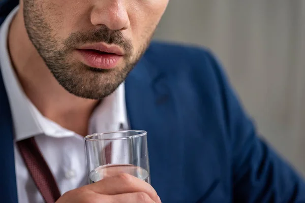 Vista ritagliata dell'uomo barbuto che tiene un bicchiere d'acqua mentre soffre di calore sul grigio — Stock Photo