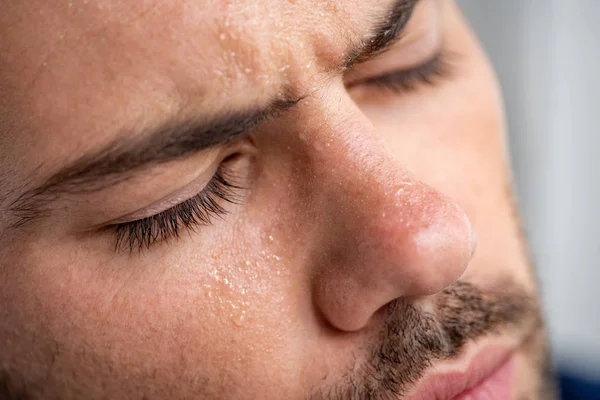 Primer plano del hombre con la cara sudorosa que sufre de calor con los ojos cerrados en gris - foto de stock