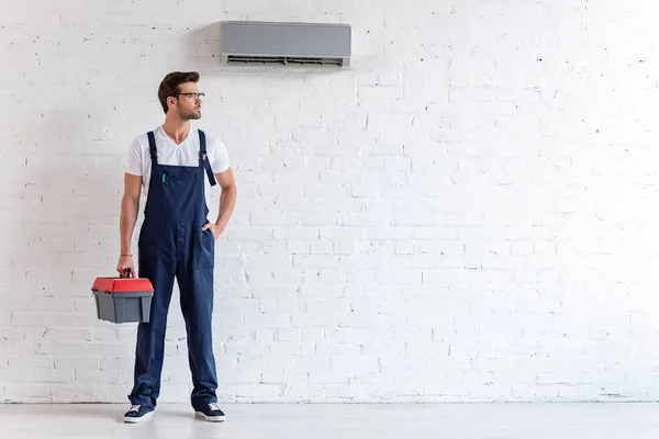 Gutaussehender Reparateur in Uniform, der unter der Klimaanlage steht und wegschaut — Stockfoto