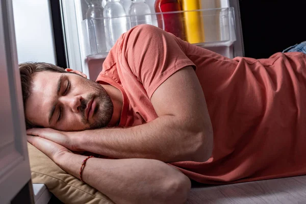 Handsome tired man sleeping on floor in kitchen near open refrigerator — Stock Photo