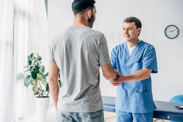 Rückenansicht des Patienten beim Händeschütteln mit dem Arzt im Massageschrank in der Klinik — Stockfoto