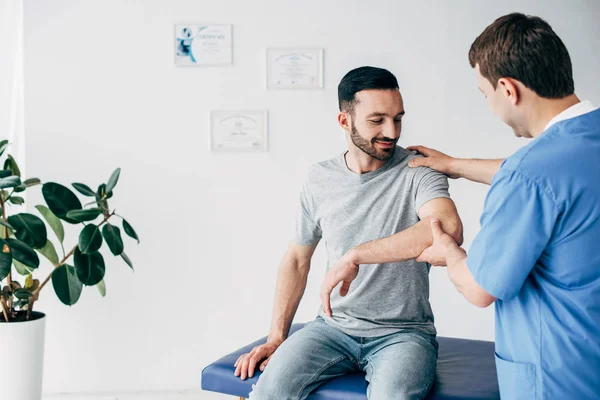 Selective focus of chiropractor examining patient shoulder in massage cabinet at clinic — Stock Photo