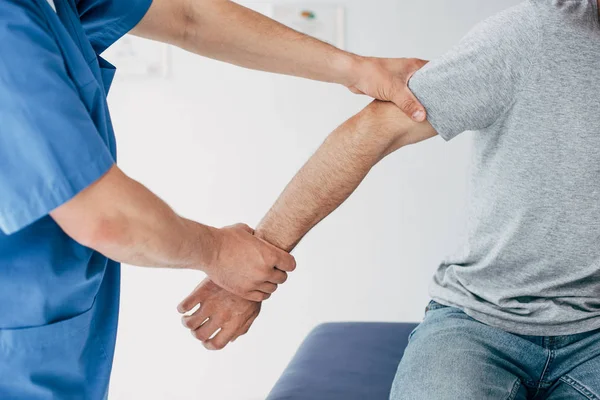 Обрезанный вид мануального терапевта, манипулирующего рукой пациента в массажном кабинете в клинике — стоковое фото