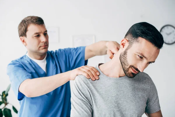 Selective focus of patient sitting on couch and doctor massaging patient neck in massage cabinet at clinic — Stock Photo