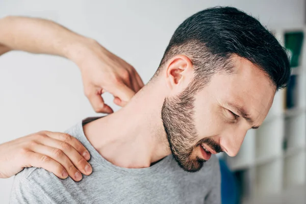 Quiroprático massageando pescoço de homem barbudo no hospital — Fotografia de Stock