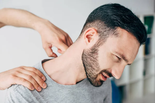 Quiropráctico masajeando cuello de hombre barbudo en hospital - foto de stock