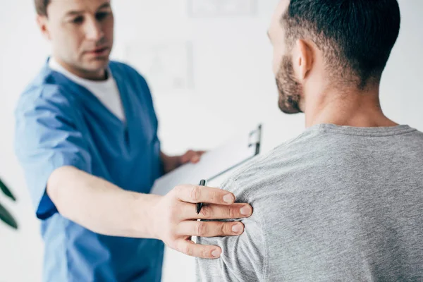 Chiropractor with diagnosis examining shoulder of man in hospital — Stock Photo
